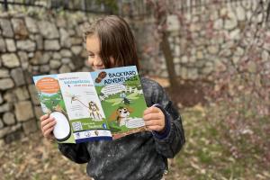 A child outside, reading a brochure titled Backyard Adventures. 