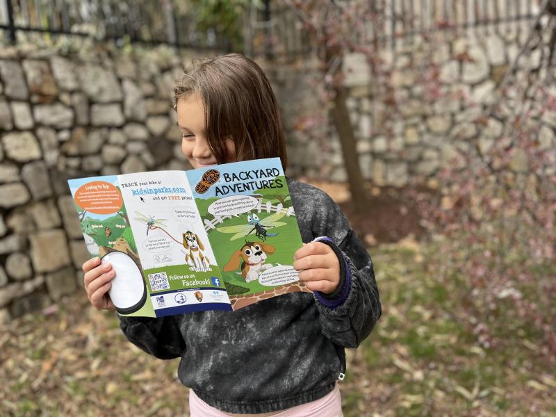Child reading brochure. A child outside, reading a brochure titled Backyard Adventures.