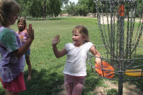 3 young girls hanging out by a disc golf basket