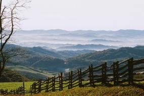 split rail fence in the foreground and rolling misty mountains in the background