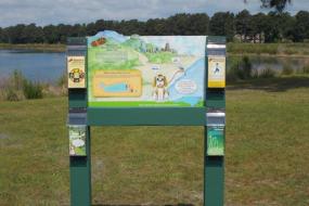 Trailhead sign with brochures in front of lake