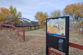 Fort Laramie TRACK Trailhead sign with iron bridge in the background
