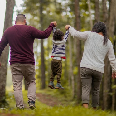 A latino family walks through the woods, swinging their child in the air.