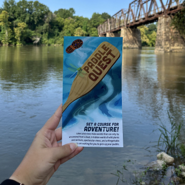 Photo of the paddle quest brochure at the edge of a river